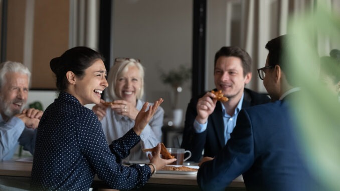 Excited diverse employees eating pizza during break in office together