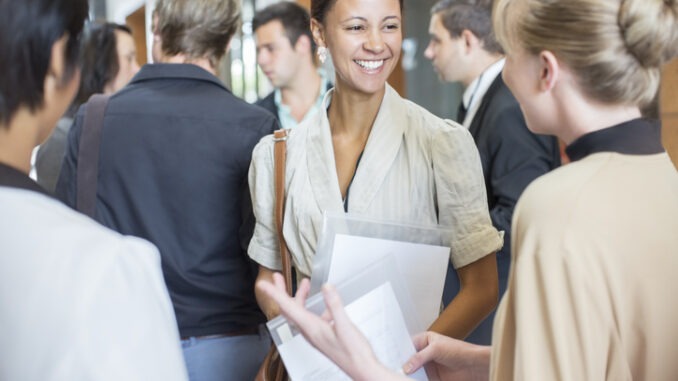 Group of conference participants standing in lobby of conference center, socializing during lunch break