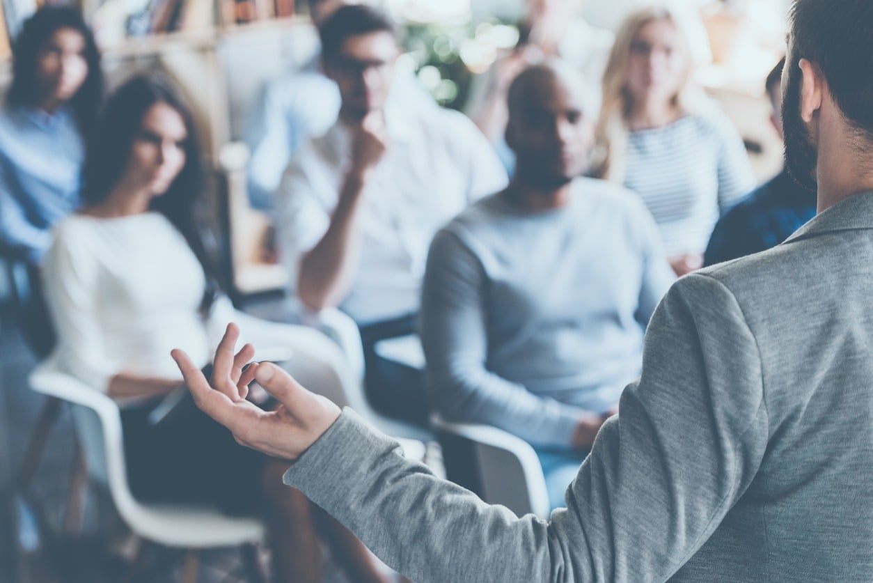 A man is talking infront of a seated audience.