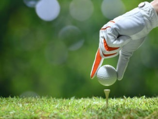 Hand hold golf ball with tee on golf course