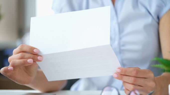 Woman reading letter while sitting at table with open envelope. Businesswoman working with correspondence received information from bank concept