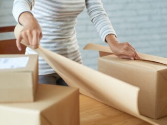 Hands of woman using craft paper to wrap giftbox or parcel