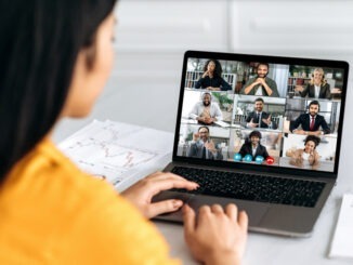 Online video conference, group brainstorm. Over shoulder view of girl on a laptop screen with group of multiracial business people talking on a video call, discussing business project, business plan