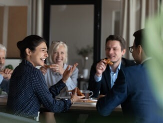 Excited diverse employees eating pizza during break in office together