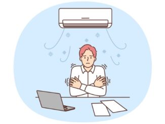 Man sitting at office desk under air conditioner freezes due to cold temperatures